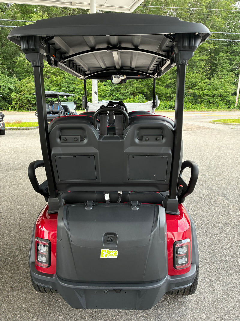 Load image into Gallery viewer, Rear view of a red and black electric golf cart parked outdoors on a paved lot with trees in the background.