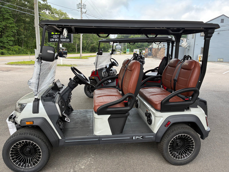 Load image into Gallery viewer, A white and black four-passenger electric golf cart with brown leather seats, parked on an outdoor paved lot. The cart features a black roof canopy, black wheels with silver spokes, and the brand name 'EPIC' visible on the side.