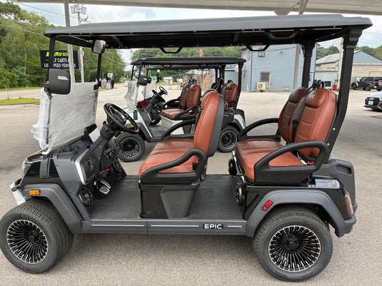 A black electric golf cart with brown leather seats, parked on an outdoor lot alongside other golf carts. The cart features a black canopy, black multi-spoke wheels, and 'EPIC' written on the side panel.
