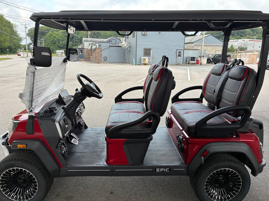 A red and black four-seat golf cart parked outdoors on a paved lot. The cart has a black roof, black seats with red stitching, black armrests, and black spoked wheels.