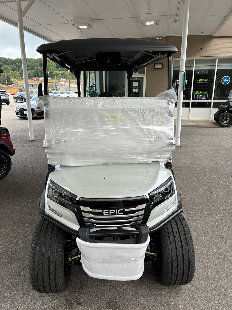 Load image into Gallery viewer, A white and black EPIC utility golf cart parked under a covered outdoor dealership area, wrapped in clear protective plastic across the upper front and windshield.
