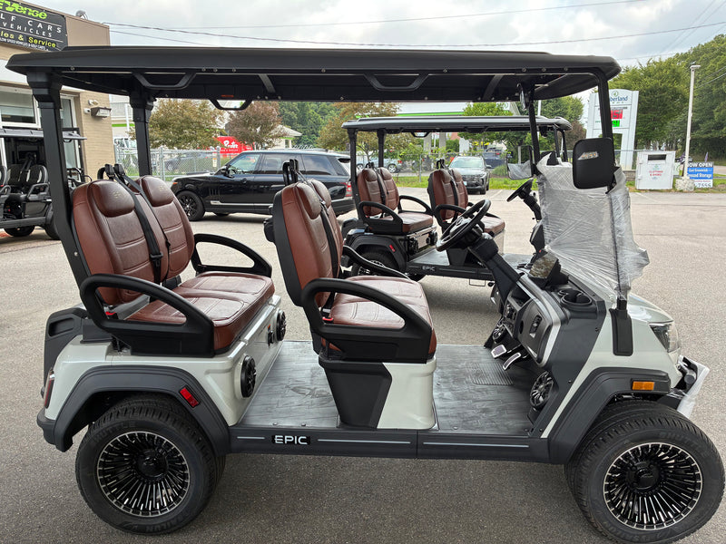 Load image into Gallery viewer, A white and black electric golf cart with brown leather seats, featuring the brand name 'EPIC' on the side, parked in an outdoor dealership lot.
