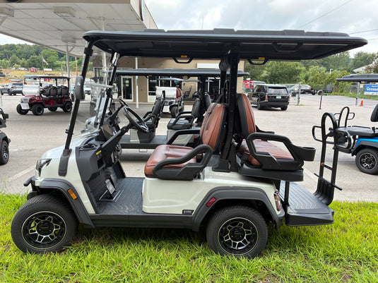 A white and black electric golf cart with brown leather seats, parked on green grass in an outdoor dealership lot.