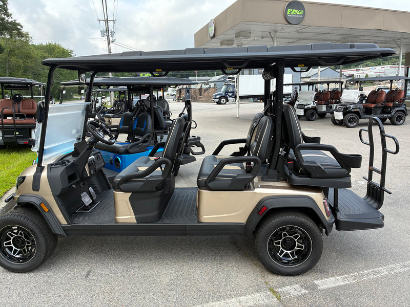 Load image into Gallery viewer, A luxury electric golf cart in champagne beige and black, photographed from the side in an outdoor dealership lot. The cart features a spacious 8-passenger layout with black bucket seats, a black roof canopy, and black wheels.
